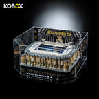 Interior tabletop decor scene with lit KGBOX display case holding LEGO 10299 Bernabéu stadium model